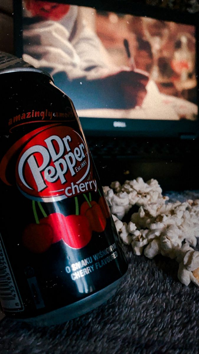 a can of soda sitting on the floor in front of a tv with popcorn scattered around it