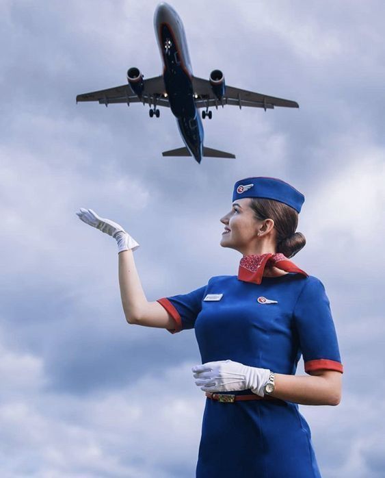 a woman dressed in an air hostess uniform is looking up at a plane flying overhead