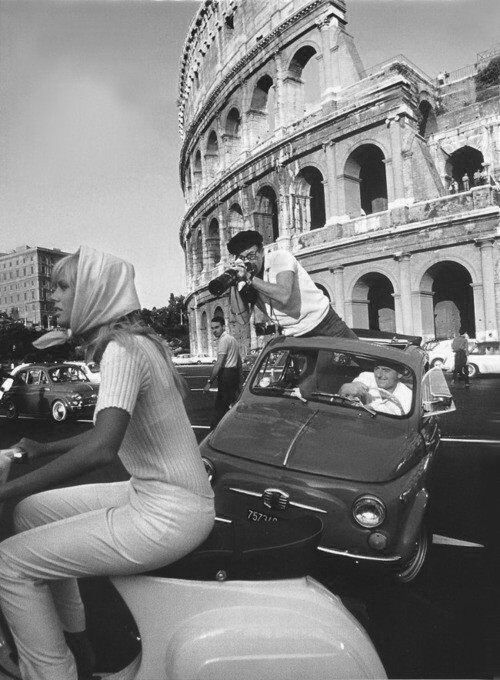 black and white photograph of people on scooters in front of the colossion