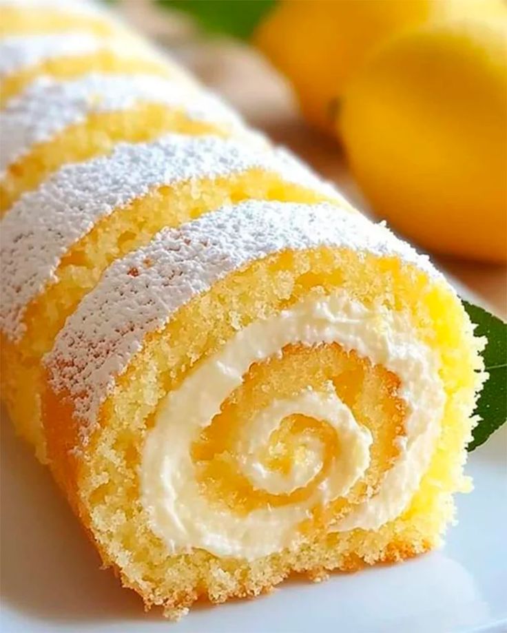 a close up of a cake roll on a plate with lemons in the background