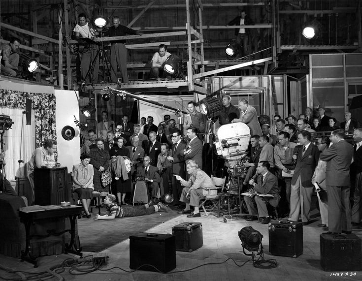 black and white photograph of people in an industrial setting with lights on the ceiling, one man is speaking