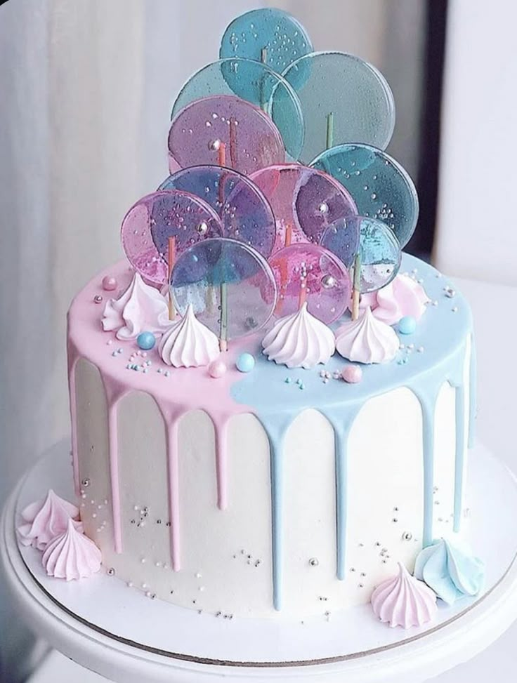 a birthday cake decorated with balloons and confetti on a white table next to a window