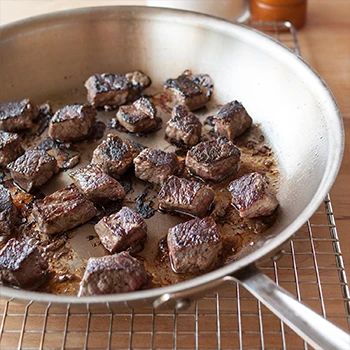 a pan filled with meat sitting on top of a table next to a glass of orange juice