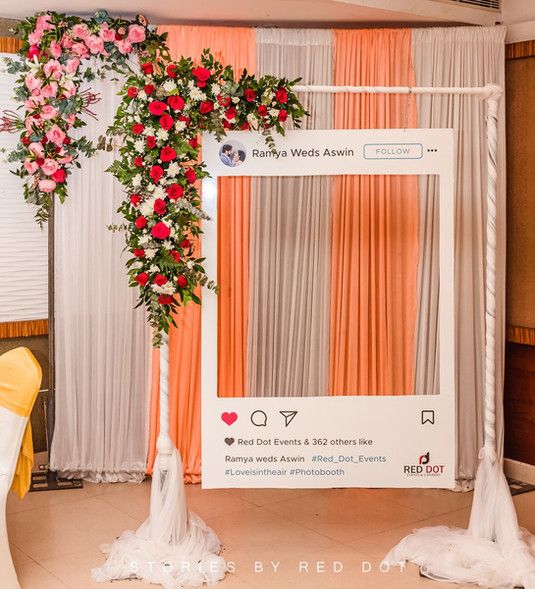 the wedding arch is decorated with red and pink flowers on it's side, along with an orange drape backdrop