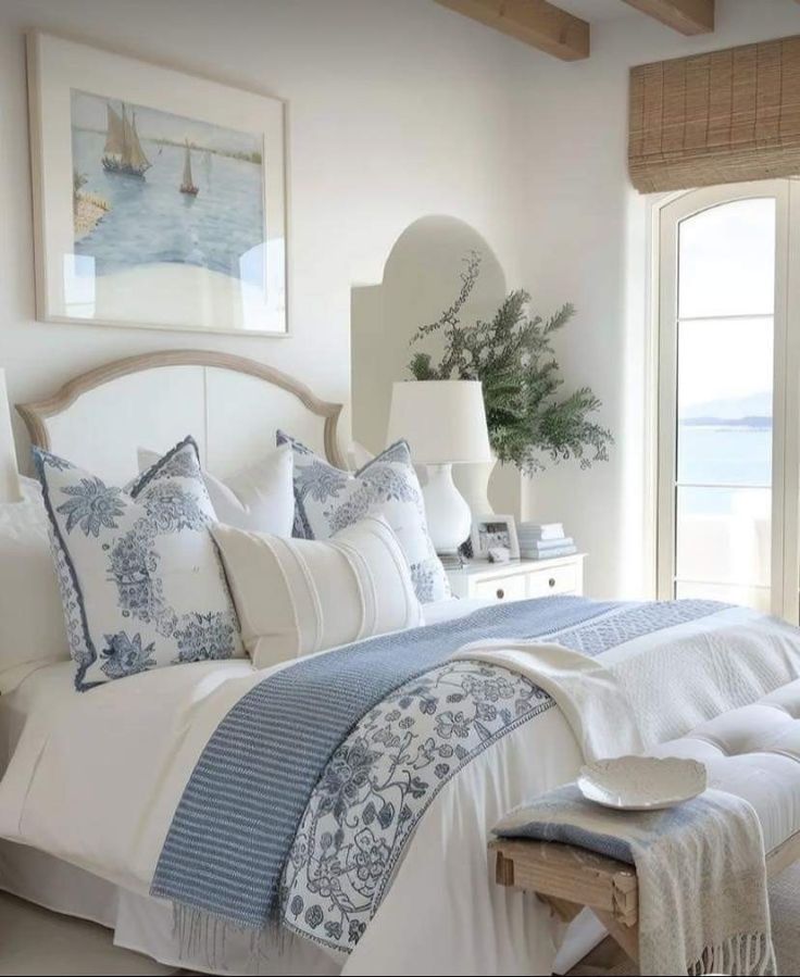 a white bed with blue and white comforter in a bedroom next to a window