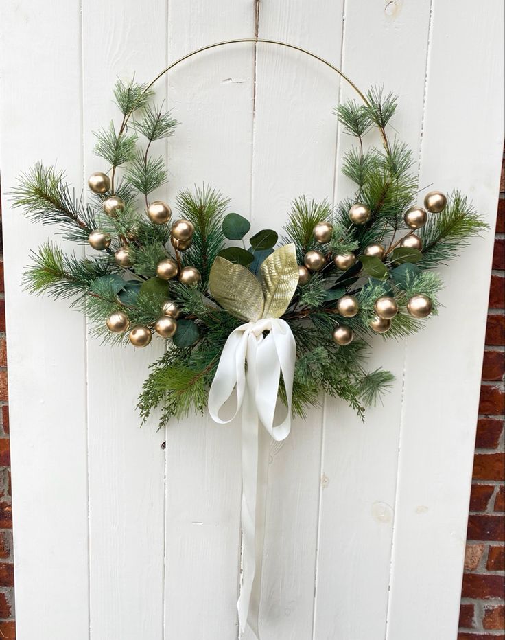 a christmas wreath hanging on the side of a white door with gold balls and greenery