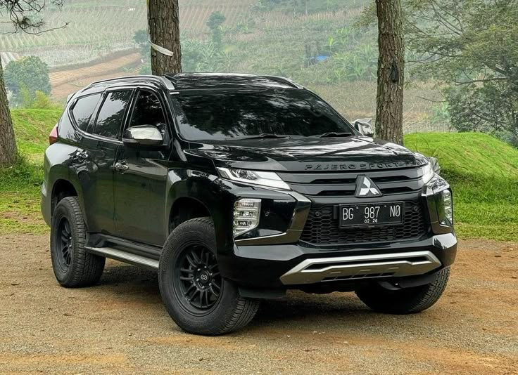 a black suv parked in the middle of a dirt road next to trees and grass