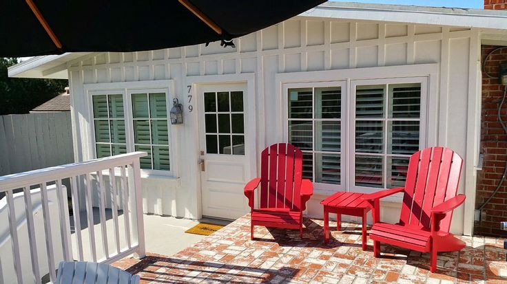 two red chairs sitting on top of a brick patio next to a white door and windows