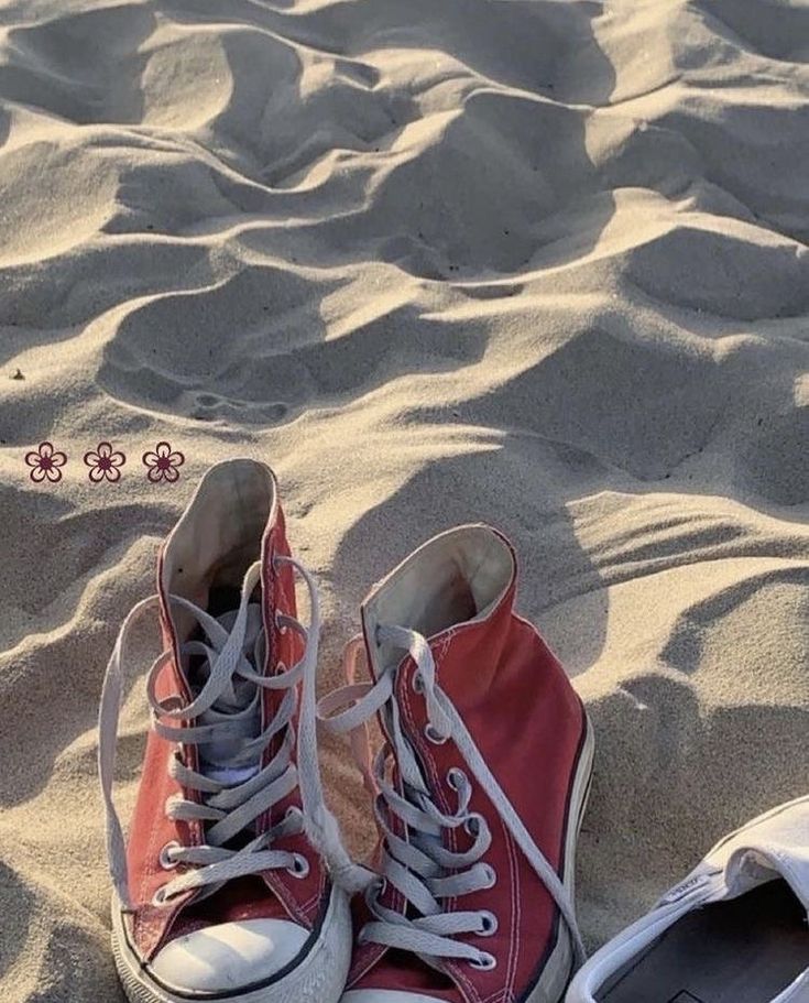 a pair of red shoes sitting on top of a sandy beach next to an object