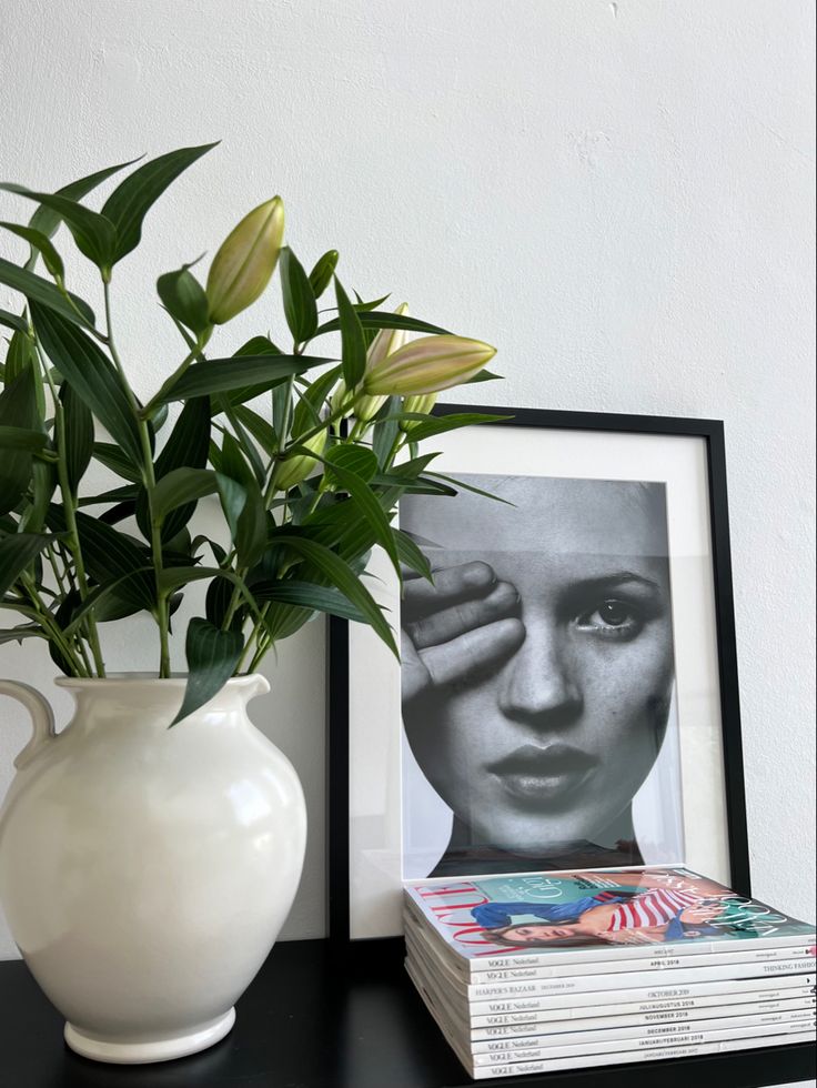 a white vase filled with green leaves next to a stack of books on a table