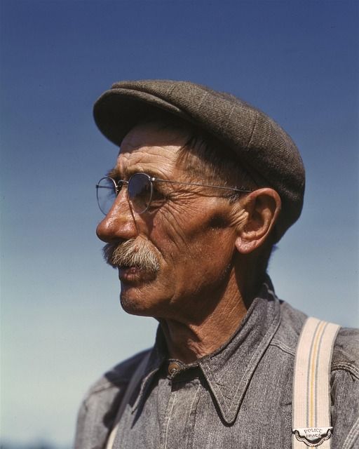 an old man with glasses and a hat is looking off into the distance while wearing suspenders