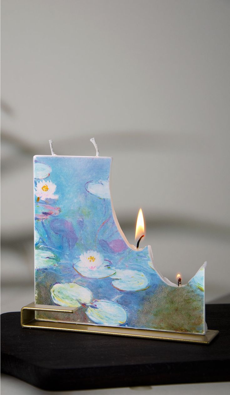 a candle that is sitting on top of a wooden block with water lillies painted on it