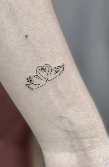 a small tattoo on the ankle of a woman's leg with two swans in it