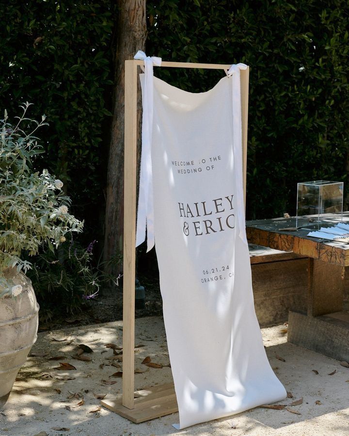 a white towel hanging from a wooden stand in front of a bush and table with potted plants