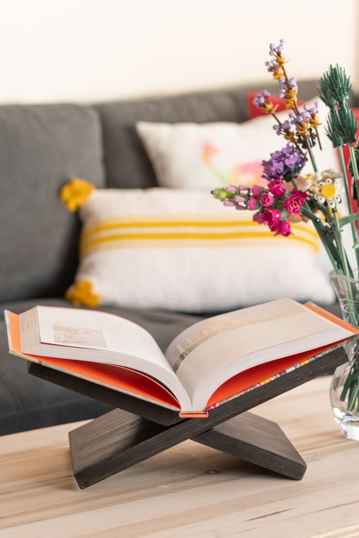 an open book sitting on top of a wooden table next to a vase with flowers