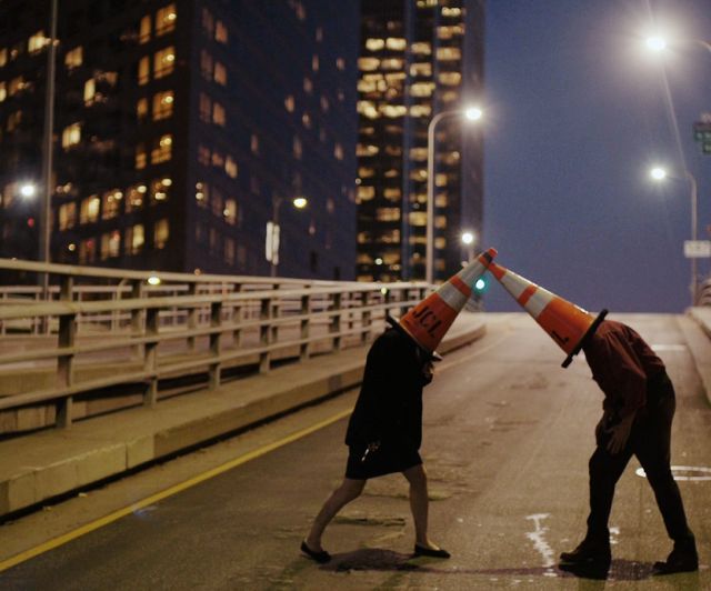 two people with traffic cones on their heads are crossing the street at night in front of tall buildings