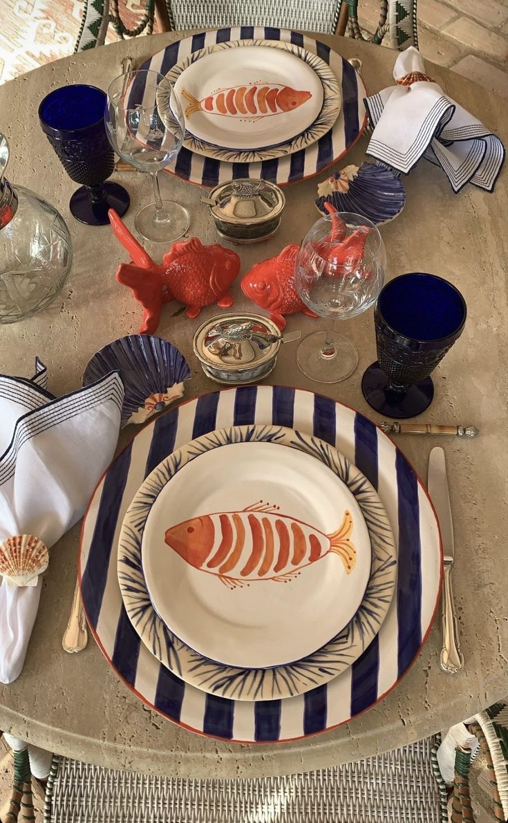 the table is set with plates, silverware and fish napkins for dinner guests