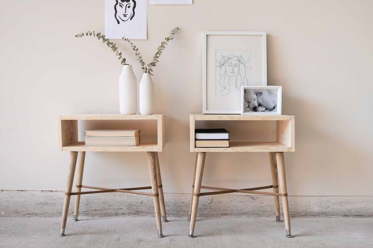 two small wooden tables sitting next to each other in front of a wall with pictures on it