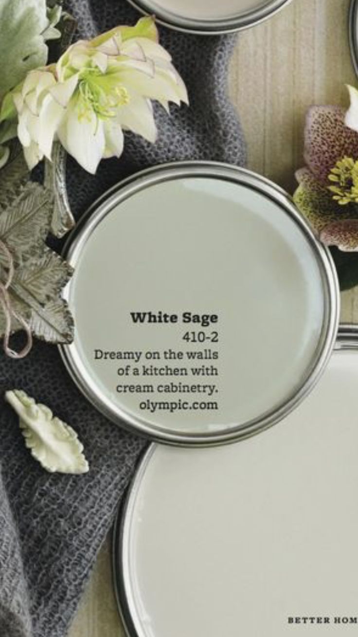 three white paint cans sitting on top of a wooden table next to flowers and leaves