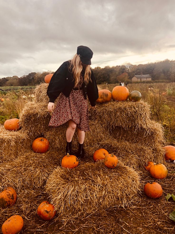 a woman standing on top of hay bales filled with pumpkins