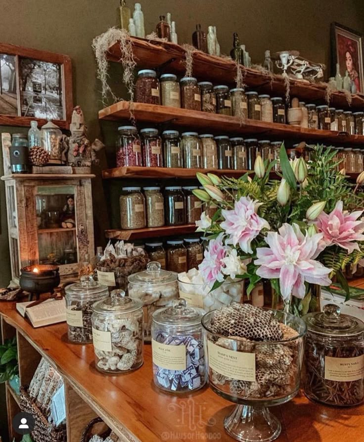 jars filled with flowers on top of a wooden table next to shelves full of jars