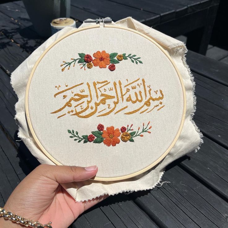 a person holding up a cross - stitched piece of cloth with the words in arabic on it