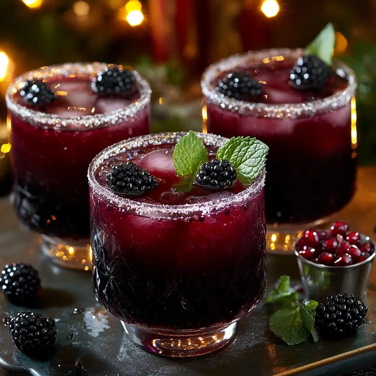 two glasses filled with red wine and blackberries on top of a metal platter