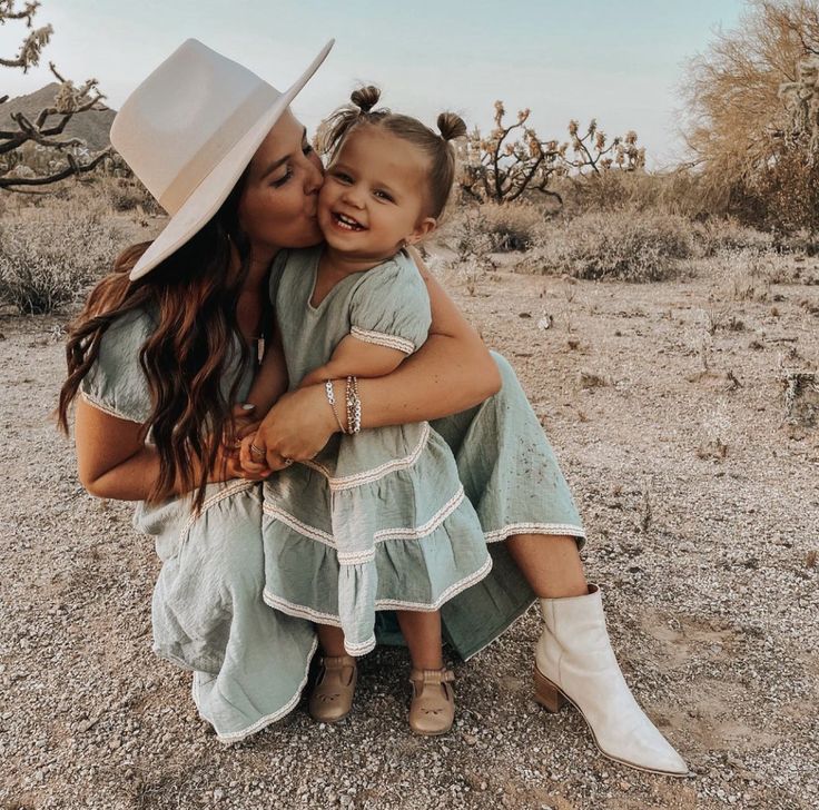 a mother and her daughter are sitting in the desert with cactus trees behind them, kissing each other