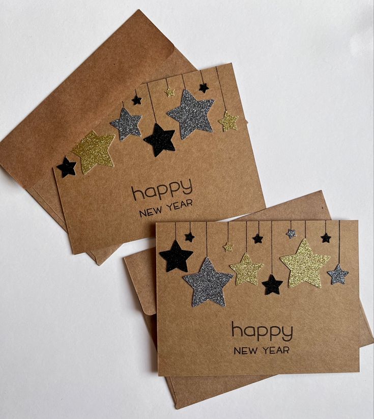 two new year's cards with gold and silver stars hanging from strings on brown paper