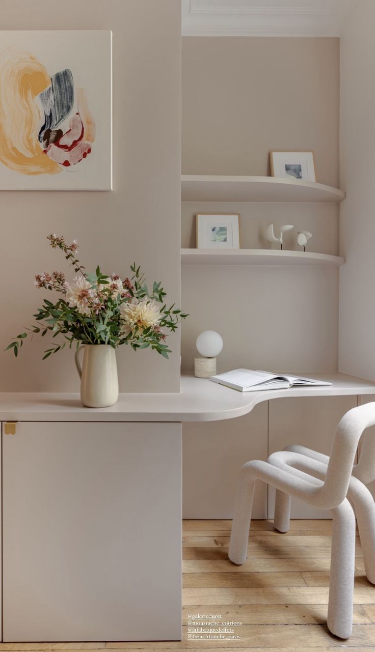 a vase with flowers sitting on top of a desk next to a chair and shelf