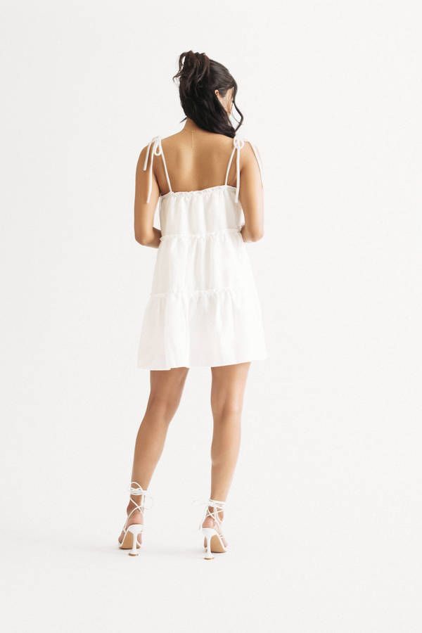 "Take Your Style Up A Notch With This Spring Fling Off White Tiered Babydoll Mini Dress. The Tiered Skirt And Ruffled Trim Add A Touch Of Fun And Flirty Vibes, While The Adjustable Tie Straps Provide A Comfortable And Custom Fit. Made From A Soft And Flowy Fabric, This Dress Is Perfect For A Day Out Or A Day In. Add Some Strappy Sandals Or Some Sneakers And You'Re Good To Go!" Flirty Mini Dress With Adjustable Ruffled Straps, White Mini Dress With Ruffled Straps, Summer Tiered Sundress With Adjustable Straps, Beach Dresses With Adjustable Straps And Tiered Shape, Beach Dresses With Adjustable Straps And Tiered Design, Summer Dress With Adjustable Straps And Tiered Shape, Spring Beach Tiered Dress With Adjustable Straps, Summer Tiered Sundress With Tie Back, Tiered Tie Back Summer Sundress