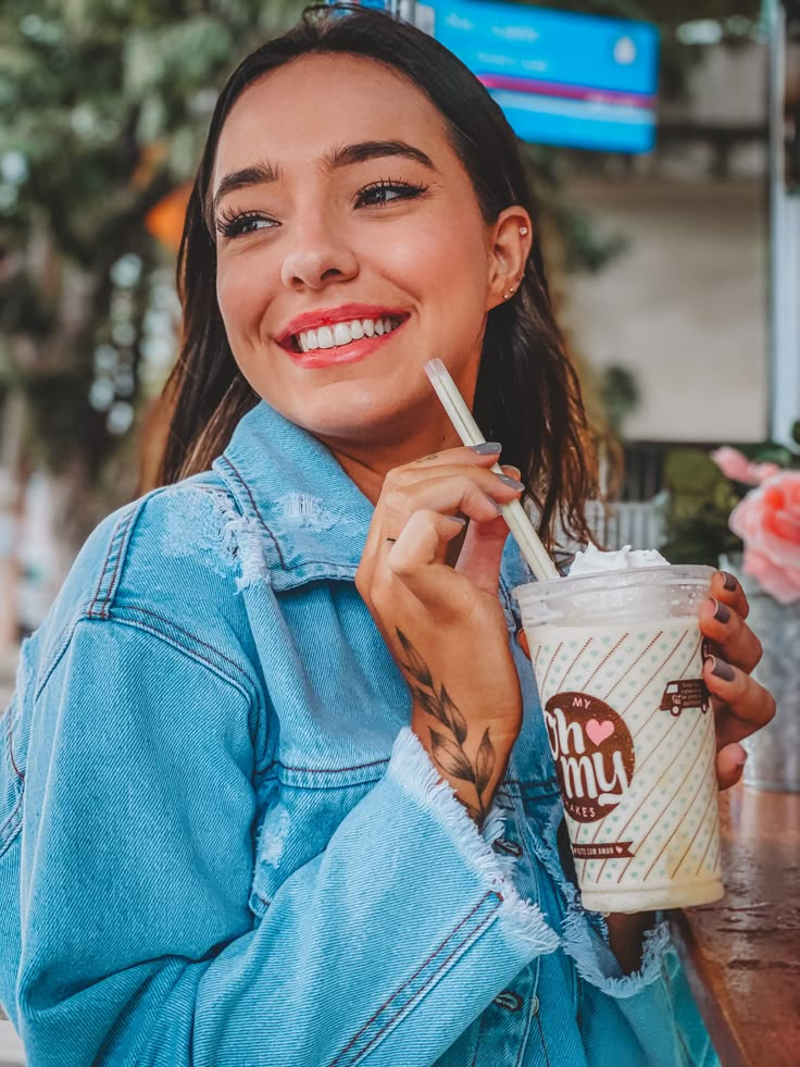 a woman is smiling while holding a drink and looking at the camera with a straw in her hand