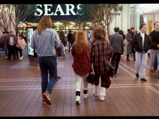 two women walking down the mall with their backs to each other, both wearing plaid shirts and jeans