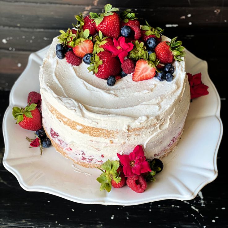 a white cake topped with fresh strawberries and blueberries on top of a white plate