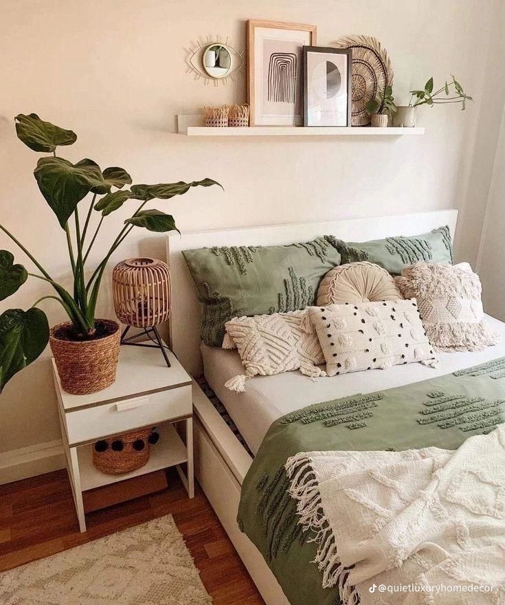 a bed with green and white pillows in a bedroom next to a potted plant