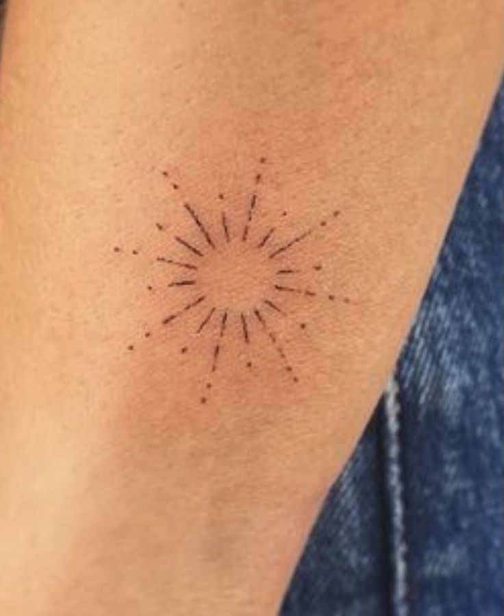 a woman's arm with a small sunburst tattoo on the left side