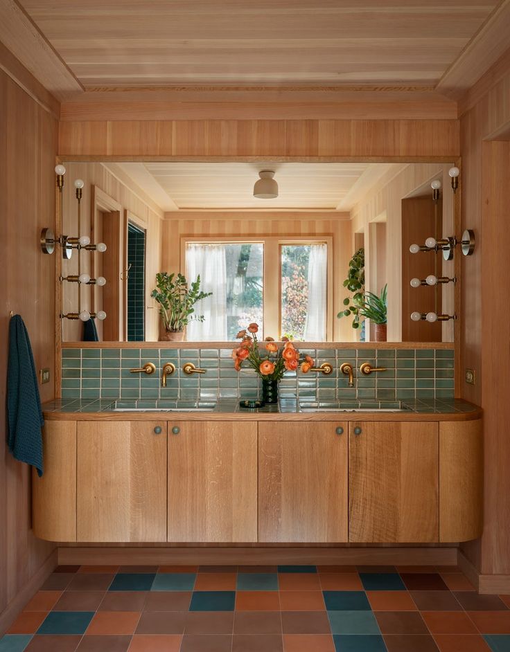 a bathroom with wooden cabinets and tile flooring in front of a large window that has potted plants on the counter