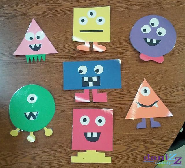 paper cut out shapes with eyes and mouths on a wooden surface, arranged in the shape of monsters