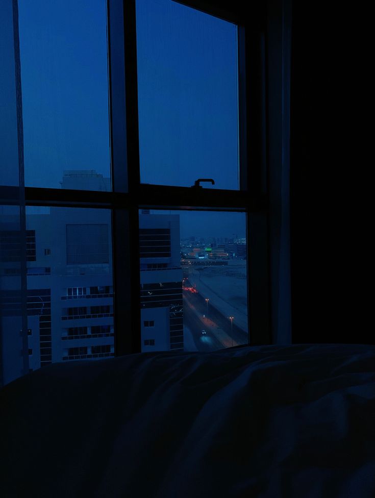 a window view of the city at night from a bed in a room with large windows