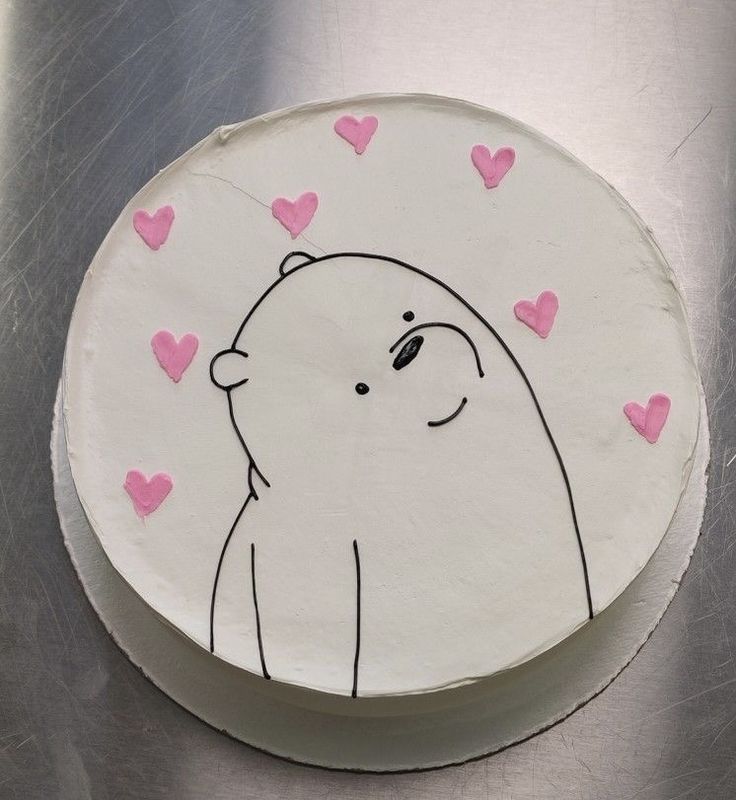 a white cake decorated with pink hearts and a polar bear on the top, sitting on a silver surface