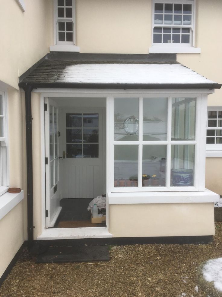 a house with white windows and snow on the ground in front of it's door