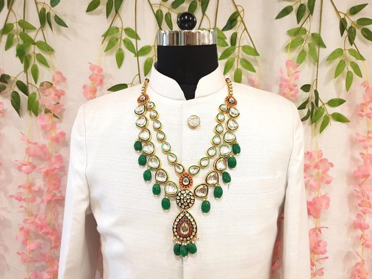 a mannequin with green and gold necklaces on display in front of pink flowers