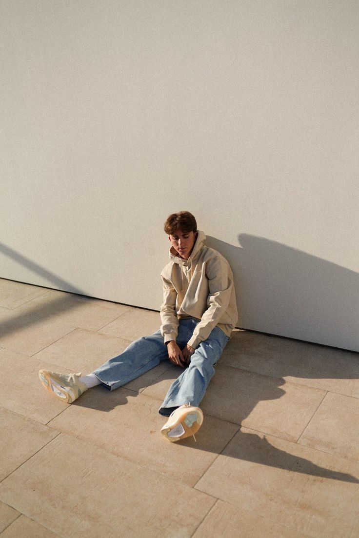 a young man sitting on the ground next to a wall