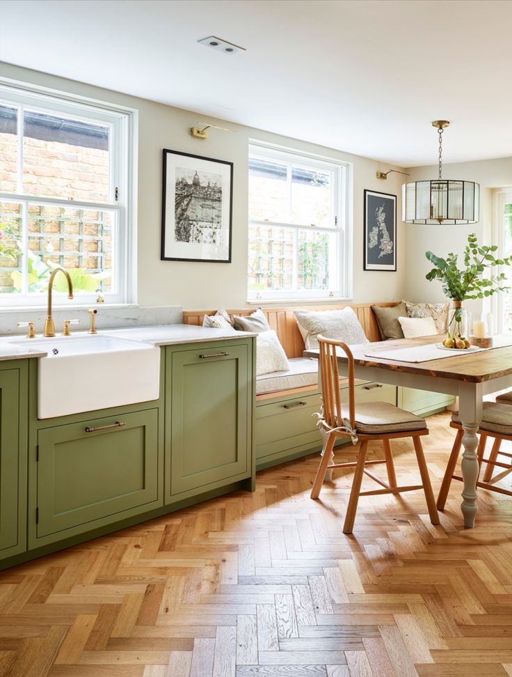 a kitchen filled with lots of green cabinets and wooden flooring next to a dining room table