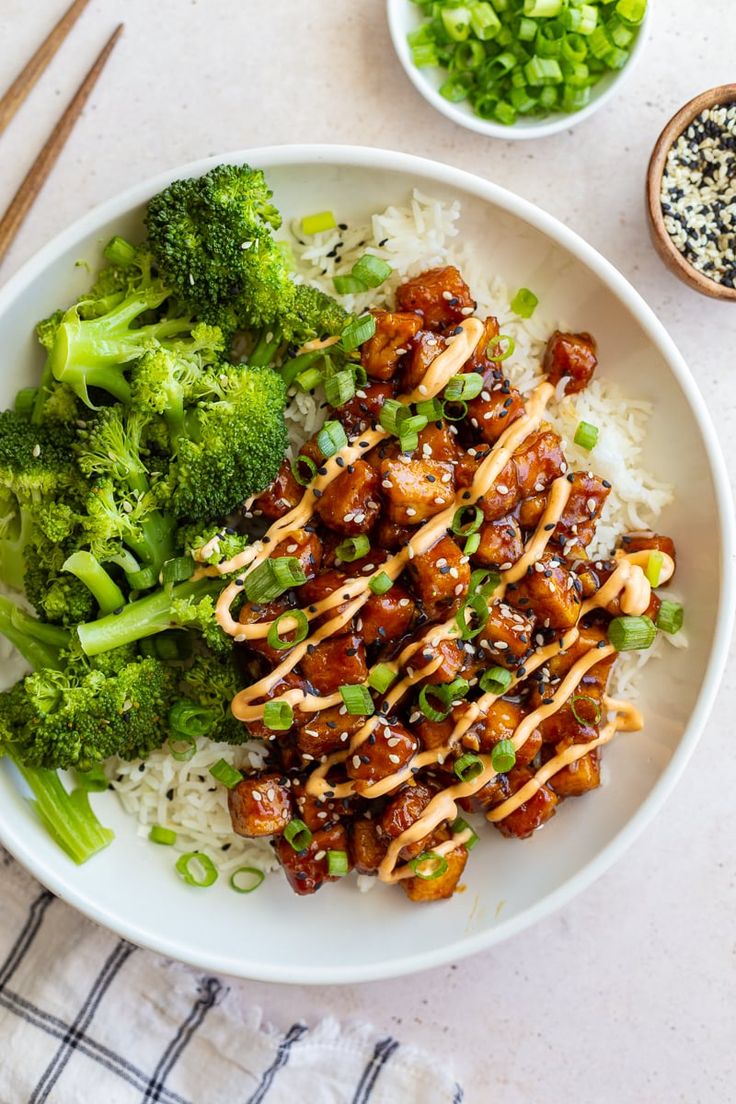 a white plate topped with rice and broccoli covered in sauce next to chopsticks