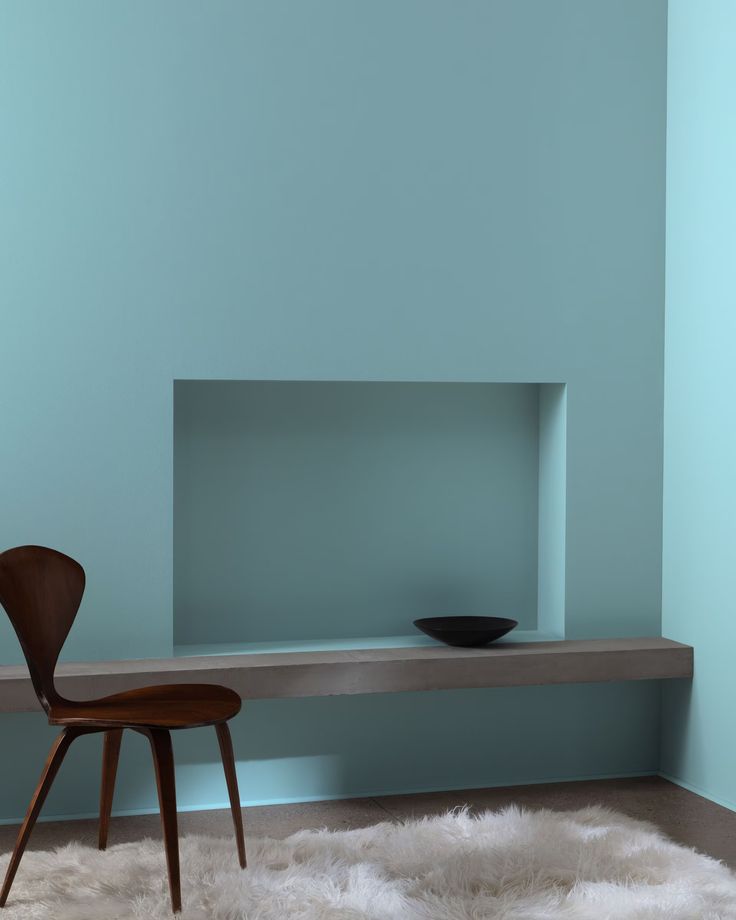 a chair sitting on top of a white rug in front of a shelf with a bowl