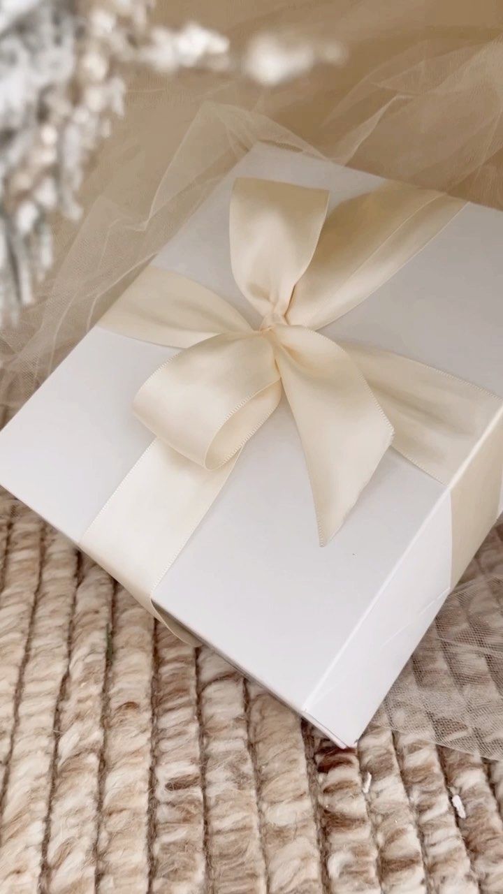 a white gift box with a bow on it sitting on a fur covered tablecloth