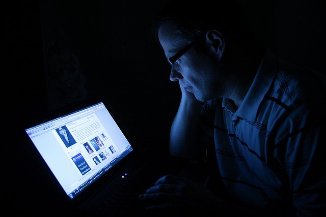 a man sitting in front of a laptop computer at night with his hand on his chin