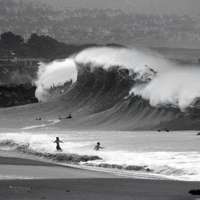 several people are surfing in the ocean with large waves behind them and buildings in the distance