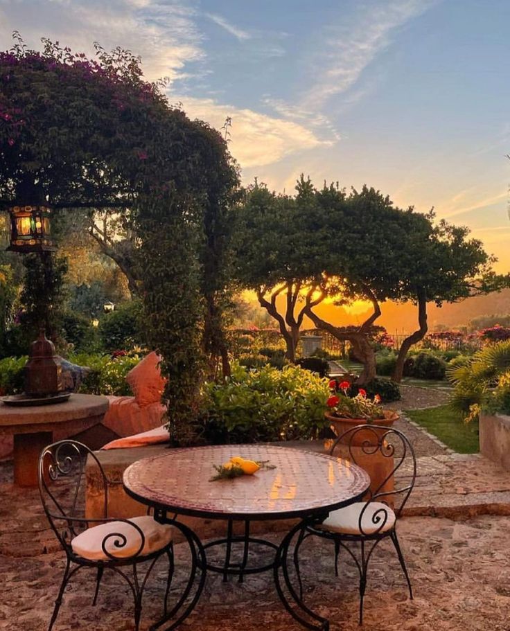 an outdoor table and chairs in front of a gazebo with trees on it at sunset